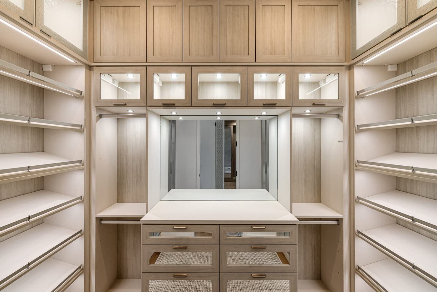 Lit walk-in closet with light oak shelving and drawers